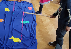 Dzieci wędkami łowią papierowe rybki – zabawa zręcznościowa.